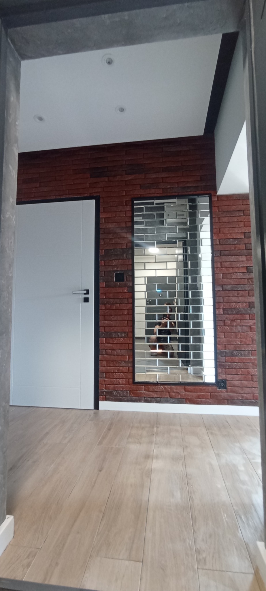 Wykończone wnętrze z ceglaną ścianą, białymi drzwiami i lustrem z efektem mozaiki. Podłoga wyłożona panelami imitującymi drewno. Widok z perspektywy podłogi.