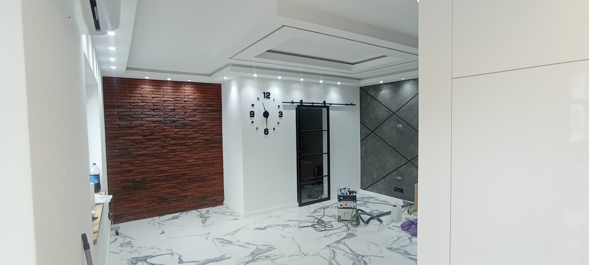 Nowoczesne wnętrze po remoncie: ceglana ściana, dekoracyjny sufit, marmurowe płytki podłogowe i przesuwne drzwi na szynie. Widoczne narzędzia malarskie.