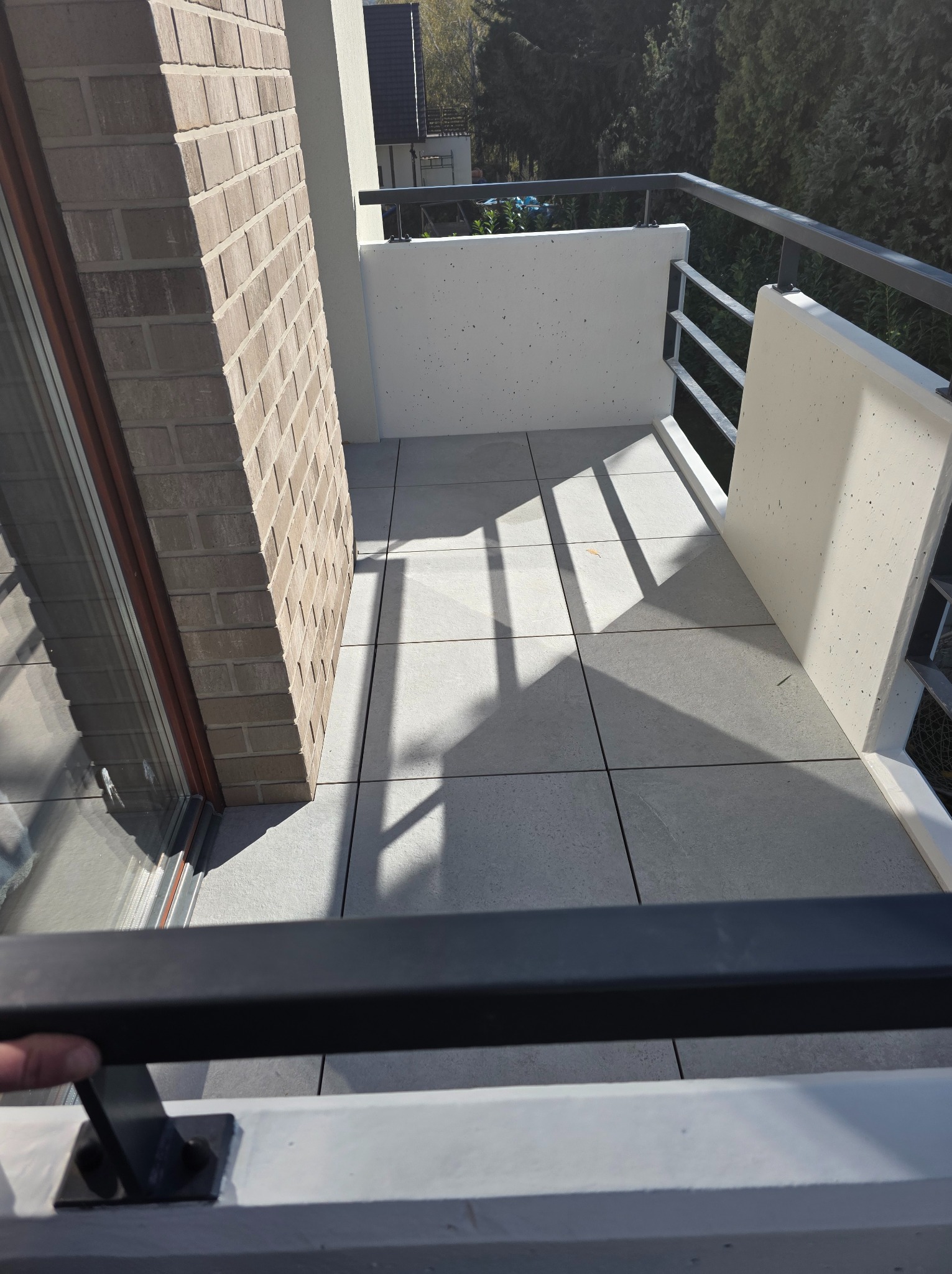 Jasnoszara, kwadratowa posadzka z płytek na balkonie z ceglanym filarem i metalową balustradą w nowoczesnym stylu, oświetlona naturalnym światłem słonecznym.