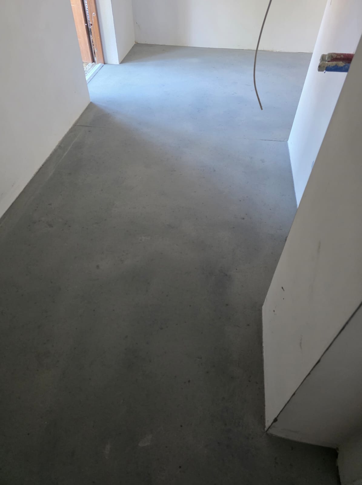 Gładka, szara posadzka w surowym wnętrzu, widoczne fragmenty ścian i instalacji. Minimalistyczny design, świeżo wylana powierzchnia, gotowa do dalszych prac wykończeniowych.