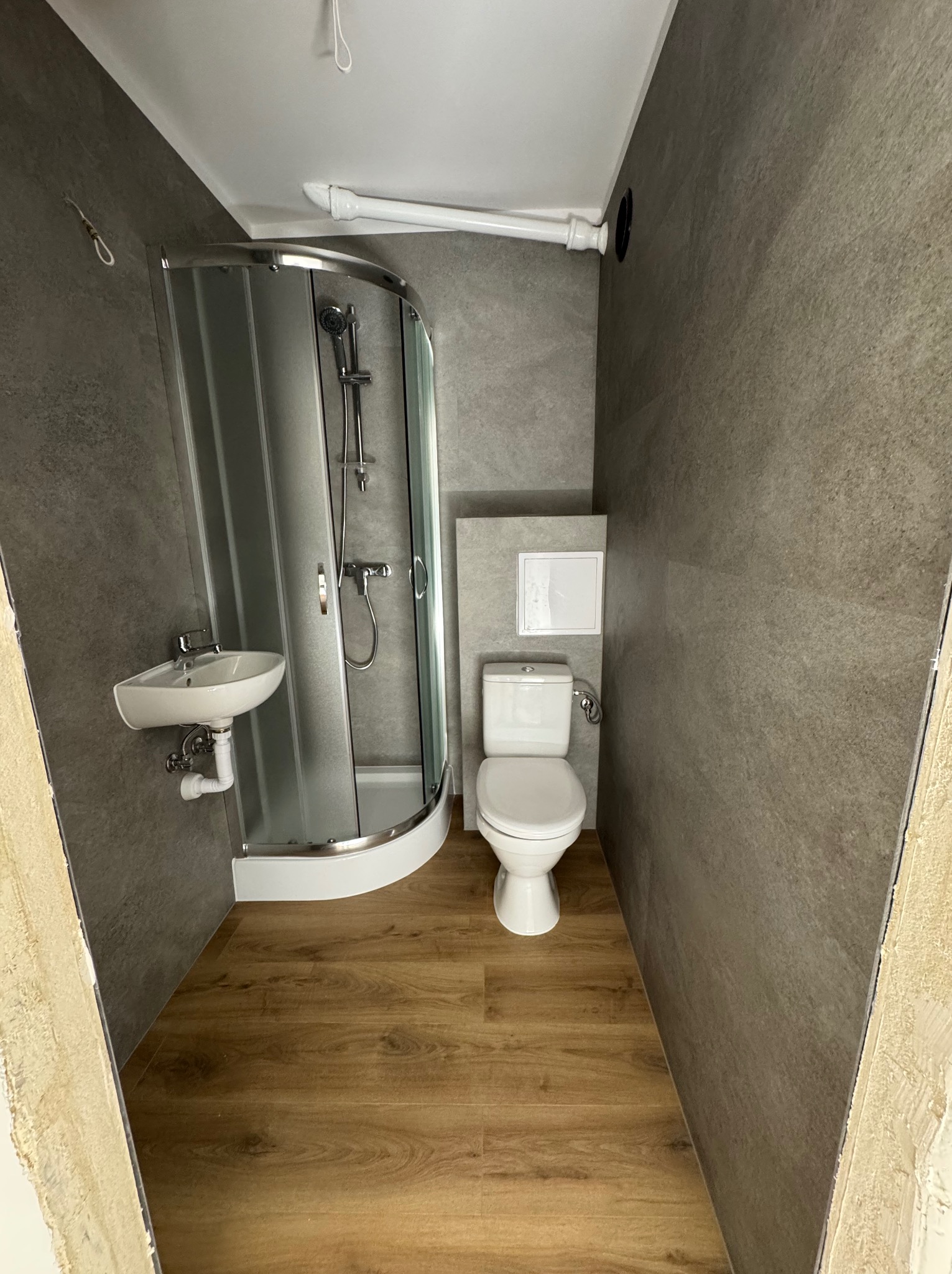 Nowoczesna łazienka po remoncie: kabina prysznicowa, umywalka i toaleta w szaro-białej kolorystyce, drewnopodobna podłoga. Widoczne detale wykończenia.