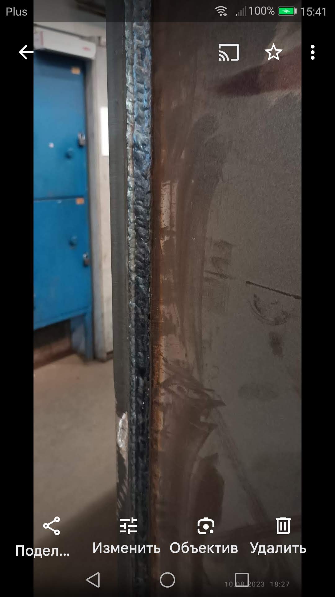 Spoina spawalnicza na metalowej konstrukcji, widoczne ślady obróbki i niedoskonałości, surowy industrialny wygląd, niebieskie drzwi w tle.