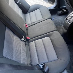 NCLEAN - mobilne pranie tapicerki - Wnętrze samochodu z widocznymi tylnymi siedzeniami z szarej tapicerki. Widoczne pasy bezpieczeństwa i elementy wykończenia wnętrza.