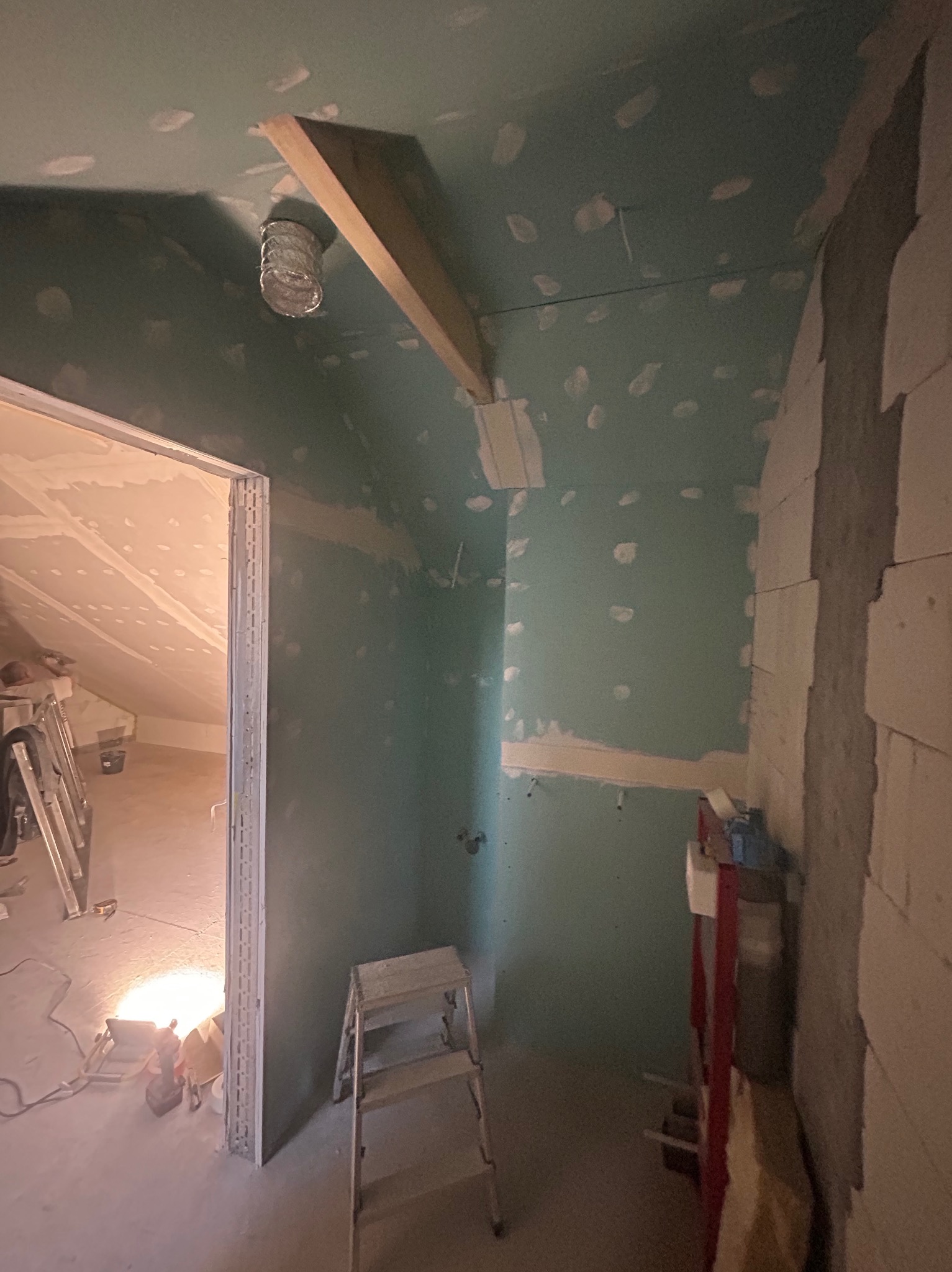 Poddasze w trakcie adaptacji: ściany z zielonej płyty gipsowej, widoczne łączenia i szpachlowanie. Fragment konstrukcji drewnianej i drabina w pomieszczeniu.