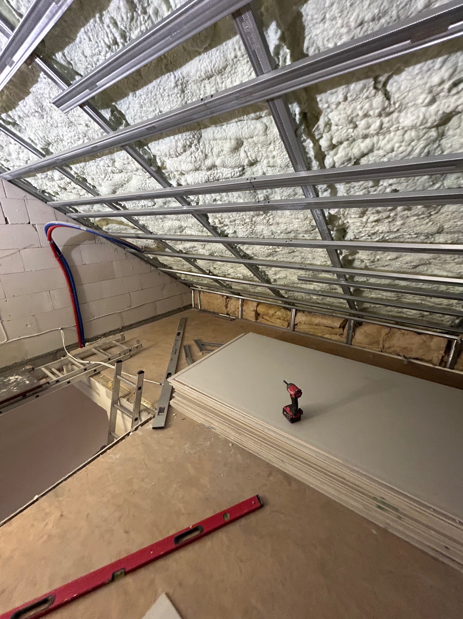 Montaż sufitu podwieszanego z płyt gipsowo-kartonowych na poddaszu. Widoczne profile, izolacja, płyty i narzędzia. Ujęcie z dołu, ukośne.