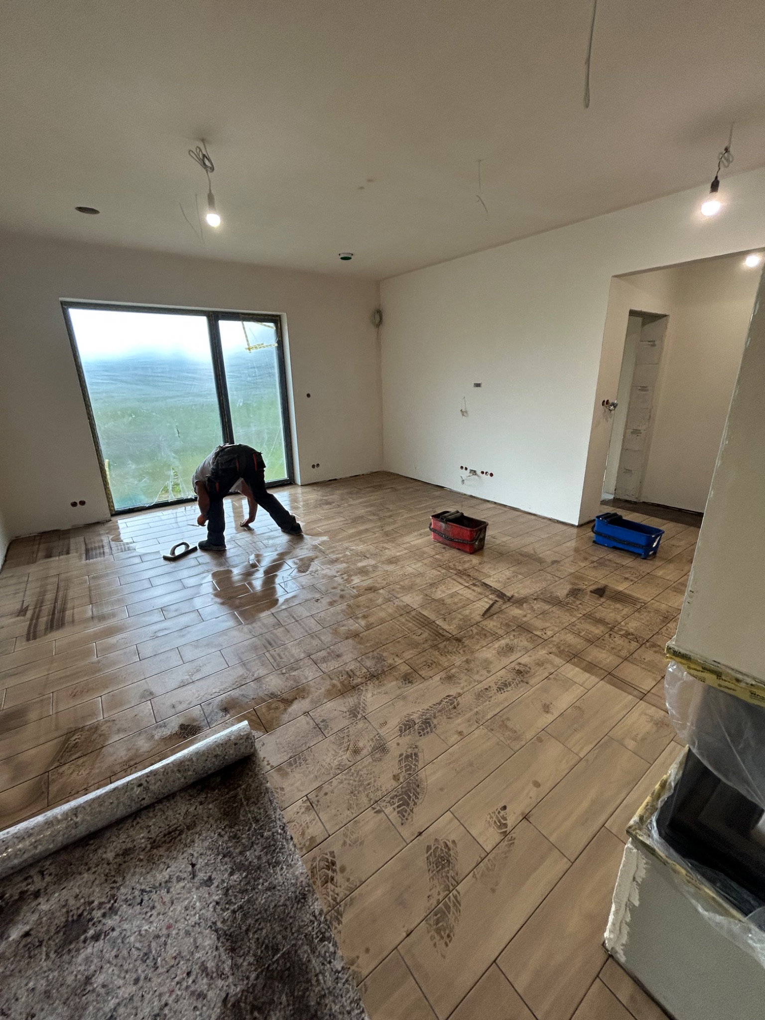 Układanie płytek podłogowych imitujących drewno w jasnym wnętrzu. Widoczne ślady na świeżo położonej podłodze i narzędzia pracy.