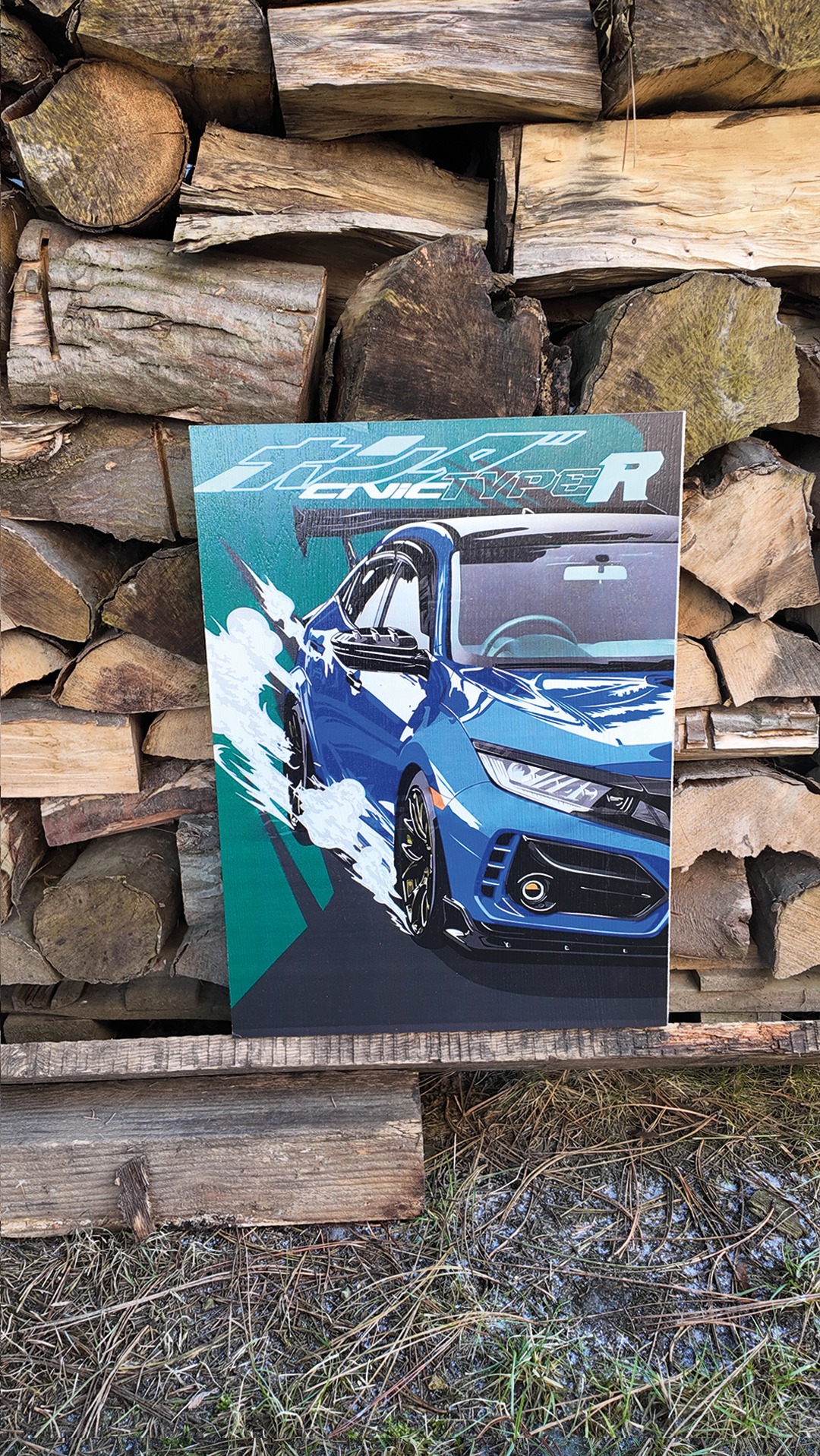 Grafika na płótnie przedstawia niebieski samochód Honda Civic Type R z efektem ruchu, umieszczona na tle stosu drewna i trawy. Wyraziste kolory i dynamiczna kompozycja.