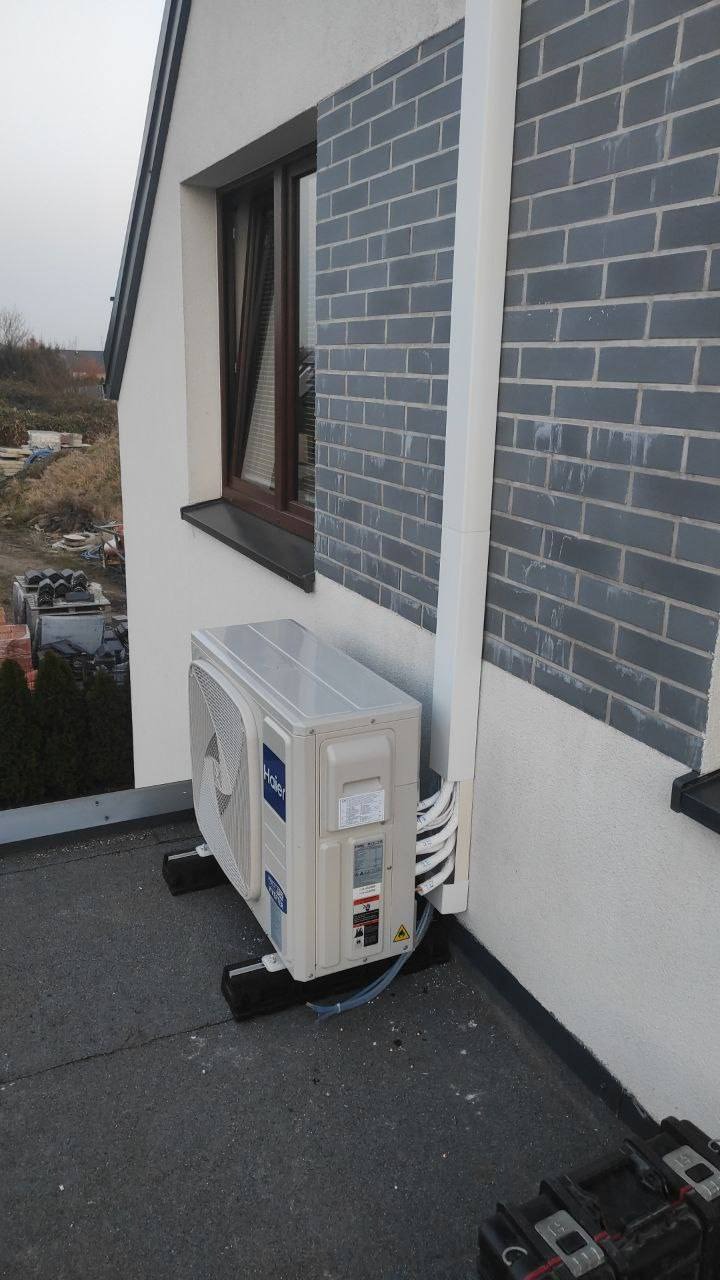 Biała jednostka zewnętrzna klimatyzacji Haier zamontowana na dachu budynku we Wrocławiu. Widoczne przewody i elementy montażowe.