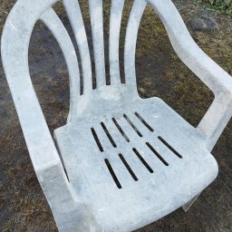 Hipnoterapia Jarosław Obrocki - Szare plastikowe krzesło ogrodowe z widocznymi śladami zabrudzeń, leżące na ziemi z resztkami trawy i kamieniami w tle. Widoczne ślady użytkowania.