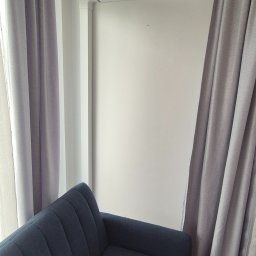 Klimator - Fragment pokoju z zasłonami i narożnikiem w odcieniach szarości i granatu. Minimalistyczne wnętrze z akcentem na tekstylia i stonowaną kolorystykę.