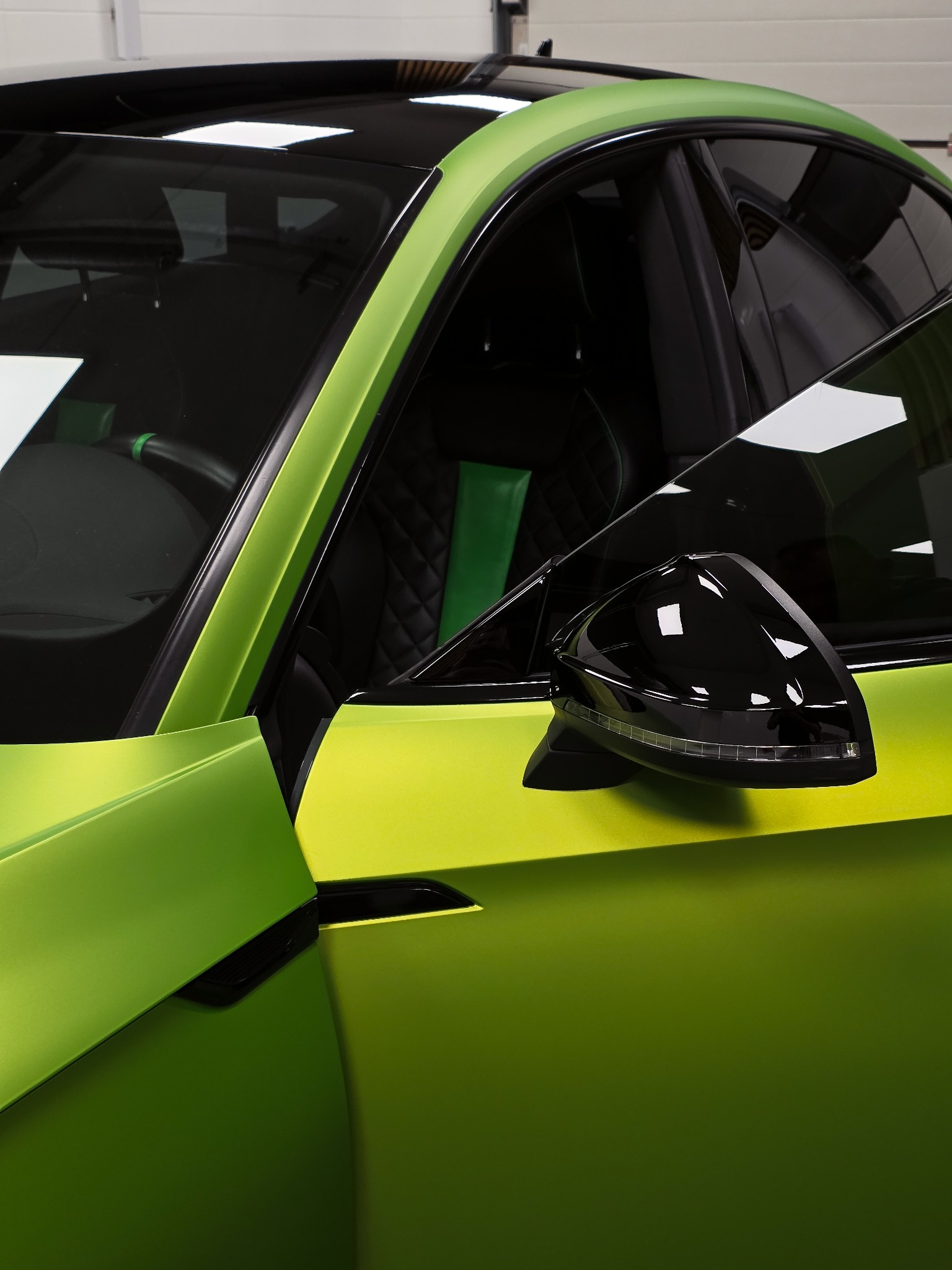 Zielony samochód po tuningu z czarnymi lusterkami i wnętrzem z zielonymi akcentami. Widoczny fragment karoserii i wnętrza.