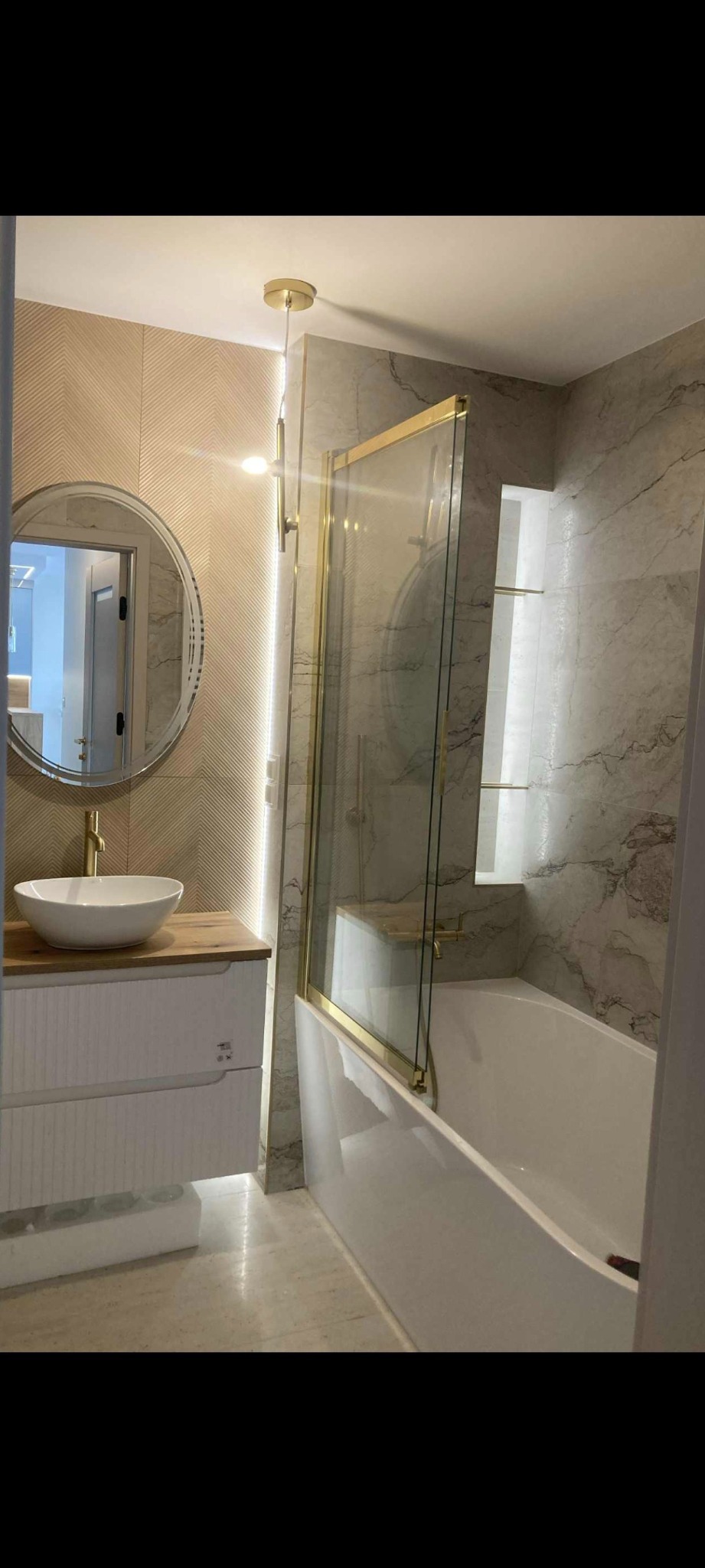 Elegancka łazienka po remoncie: biała umywalka nablatowa, złota armatura, kabina prysznicowa ze złotymi ramami i marmurowe płytki. Nowoczesny design z oświetleniem LED.