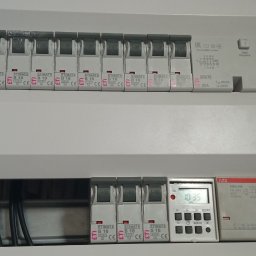 Rozdzielnica elektryczna z zamontowanymi bezpiecznikami ETIMAT i programatorem czasowym ABB, widoczne przewody. Ujęcie z bliska, oświetlenie naturalne.