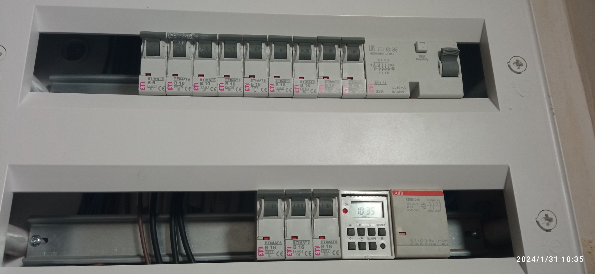 Rozdzielnica elektryczna z zamontowanymi bezpiecznikami ETIMAT i programatorem czasowym ABB, widoczne przewody. Ujęcie z bliska, oświetlenie naturalne.