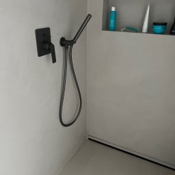 PHOTOPORT.TECH MACIEJ JAWORSKI - Minimalistyczna łazienka z szarą, gładką powierzchnią ścian i podłogi, czarną armaturą prysznicową i wnęką z kosmetykami. Nowoczesny design.