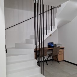 PHOTOPORT.TECH MACIEJ JAWORSKI - Białe schody z czarną balustradą w nowoczesnym wnętrzu. Widoczny fragment biurka z komputerem i krzesłami. Minimalistyczny design, jasne oświetlenie.
