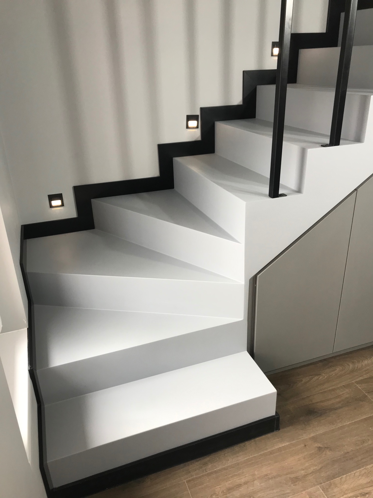 Białe schody z czarnymi akcentami i oświetleniem LED, minimalistyczny design, widok z dołu, drewnopodobna podłoga, nowoczesne wykończenie.