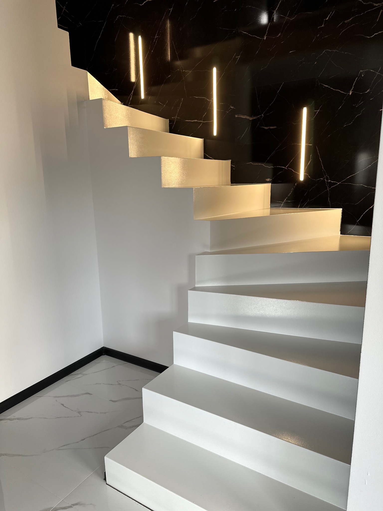 Białe schody z oświetleniem LED na czarnym tle imitującym marmur, widok z dołu. Minimalistyczny design, nowoczesne wykończenie wnętrza.