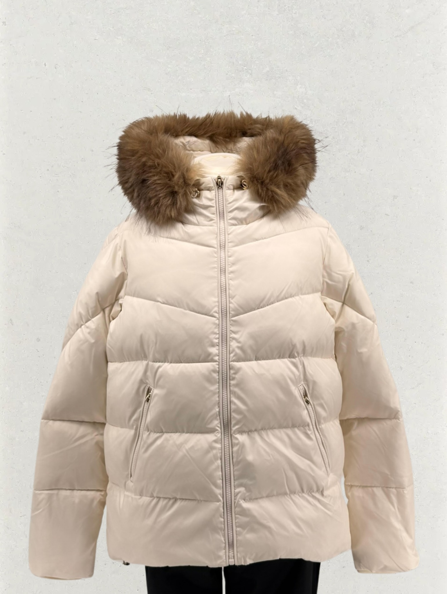 Beżowa, pikowana kurtka puchowa z kapturem obszytym brązowym futrem, zapinana na zamek błyskawiczny, widoczne kieszenie na suwak.