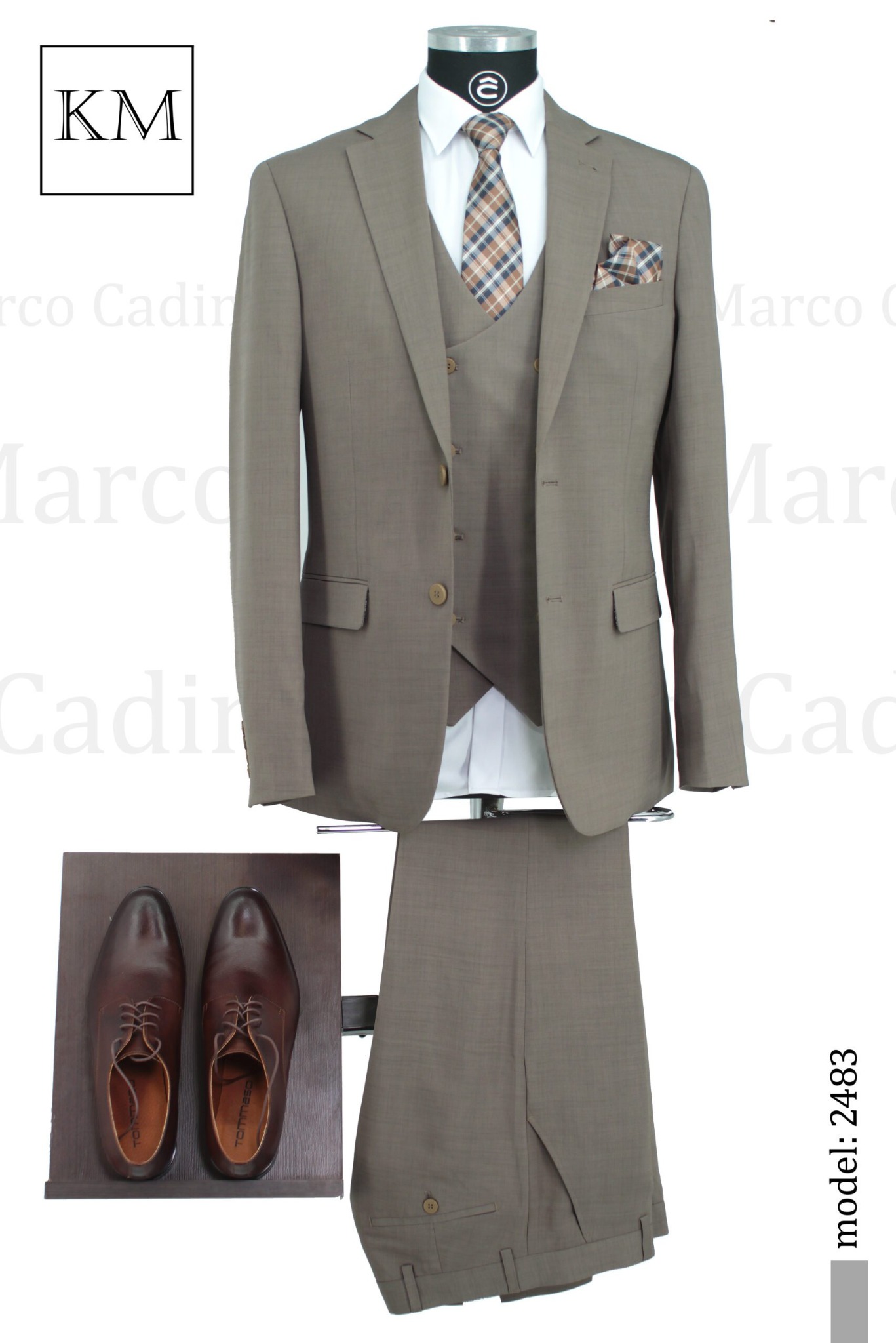 Elegancki, beżowy garnitur trzyczęściowy z brązowymi butami na ekspozycji. Widoczna koszula, krawat w kratę i poszetka. Model 2483.