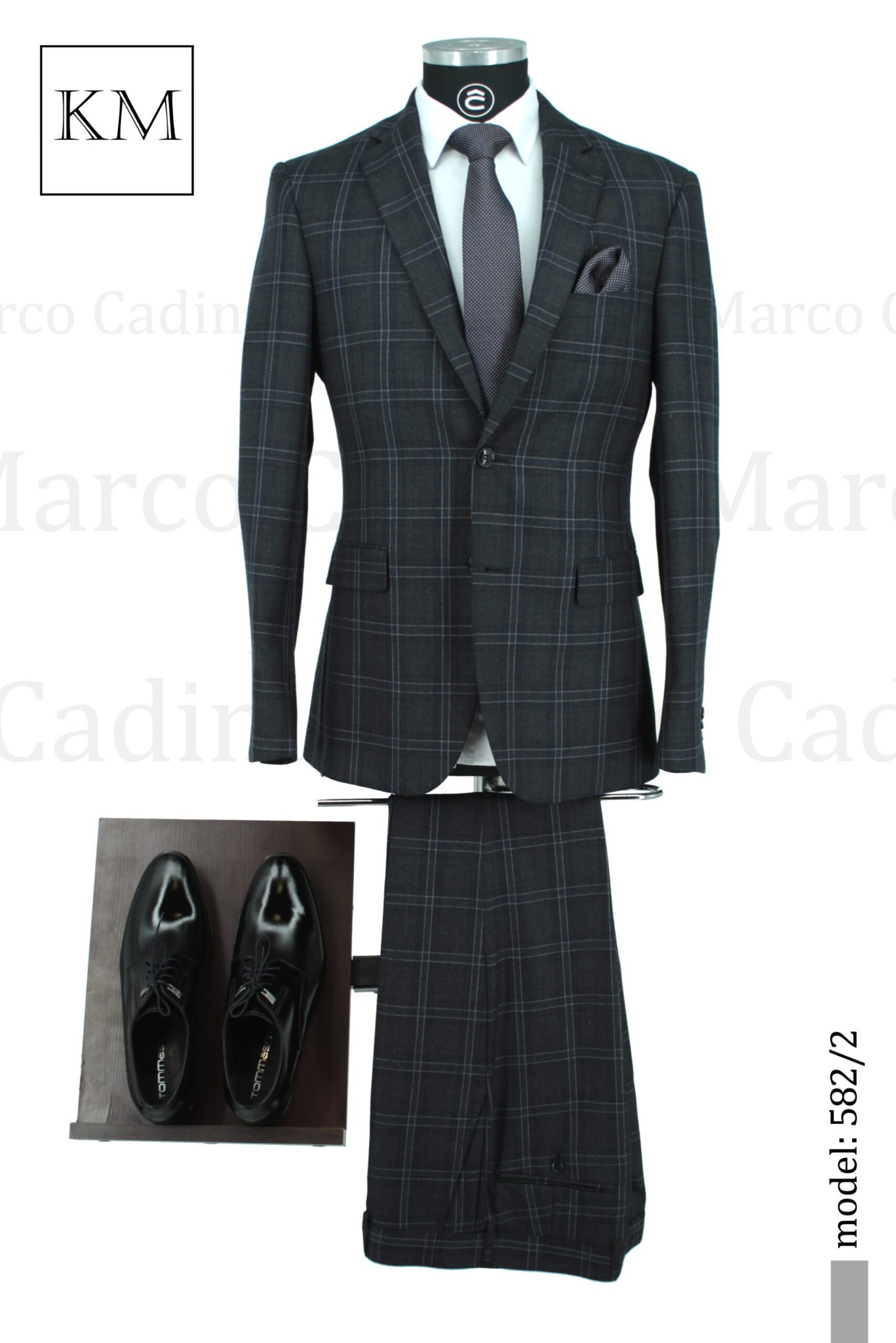 Elegancki, grafitowy garnitur w kratę, z poszetką i krawatem, prezentowany na manekinie z czarnymi, lakierowanymi butami. Model 582/2.