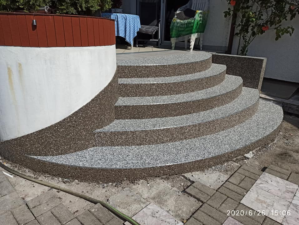 Schody zewnętrzne z żywicy epoksydowej w odcieniach szarości i brązu, z widoczną strukturą kamyczkową. Wykończenie balkonu z roślinami w tle. Data wykonania: 2020/6/26.