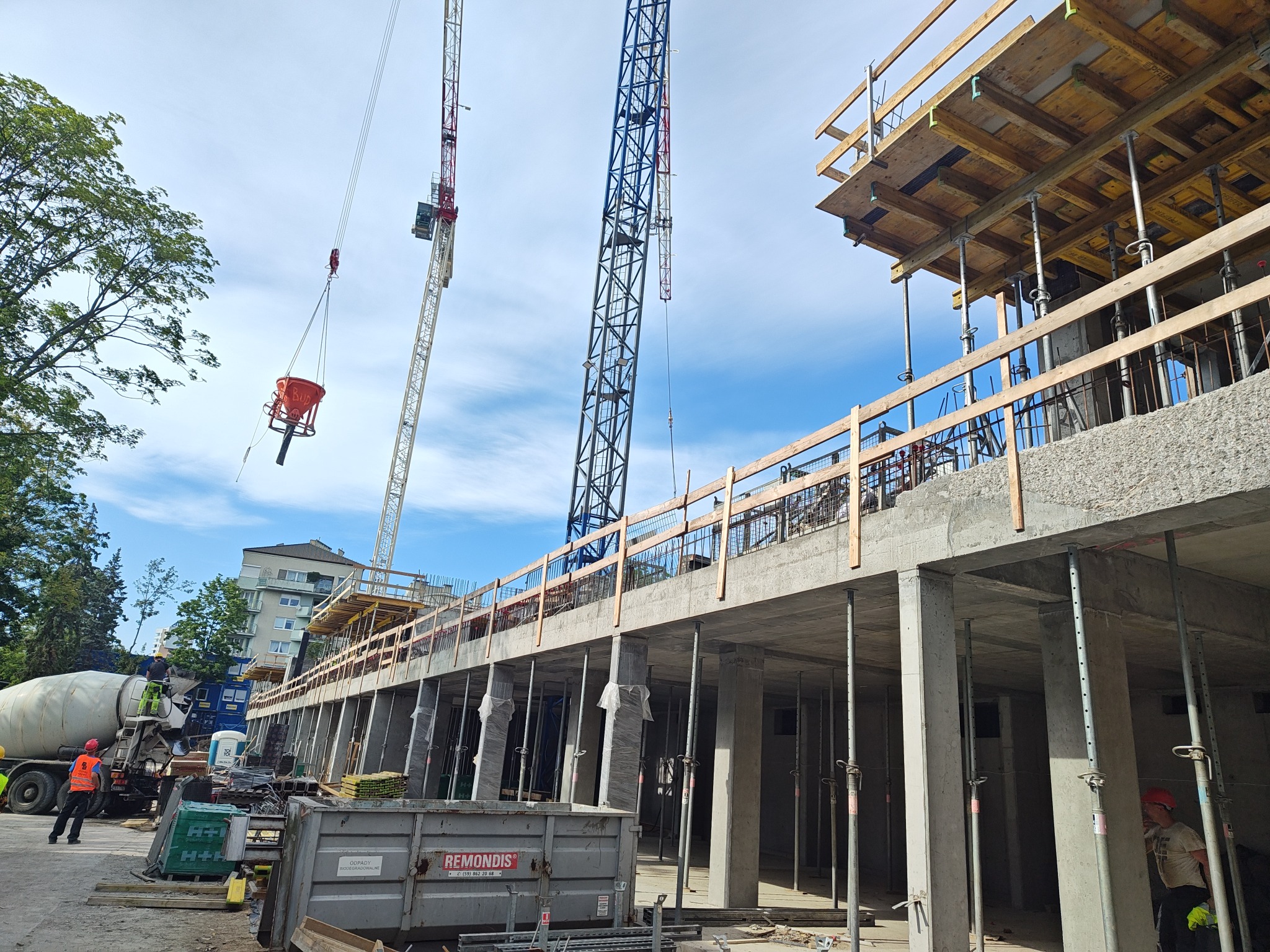 Budowa budynku żelbetowego w toku: widoczne szalunki, zbrojenia, betonowe słupy, dźwigi i betoniarka. Etap wznoszenia konstrukcji, praca wre.