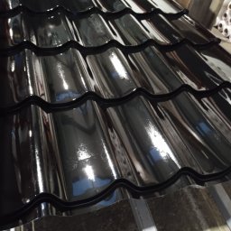 Transblach Jan Rusin - Błyszczące, czarne dachówki ceramiczne ułożone na konstrukcji dachu. Widoczne odbicia światła na powierzchni dachówek, podkreślające ich gładką fakturę.