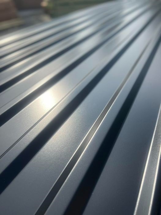 Szare, metalowe pokrycie dachowe z wyraźnymi przetłoczeniami, uchwycone pod kątem, z widocznym odbiciem światła słonecznego na powierzchni.