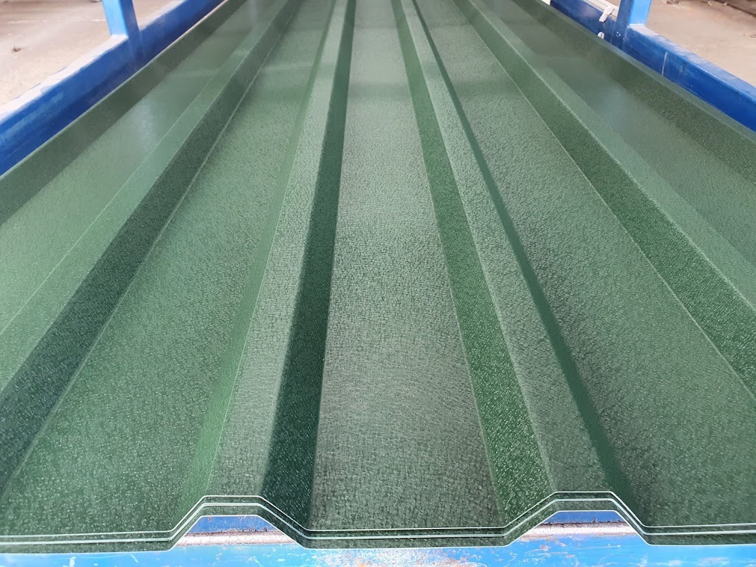 Zielona blacha trapezowa z wyraźną fakturą, ułożona na niebieskiej konstrukcji. Widoczne regularne przetłoczenia i matowe wykończenie.