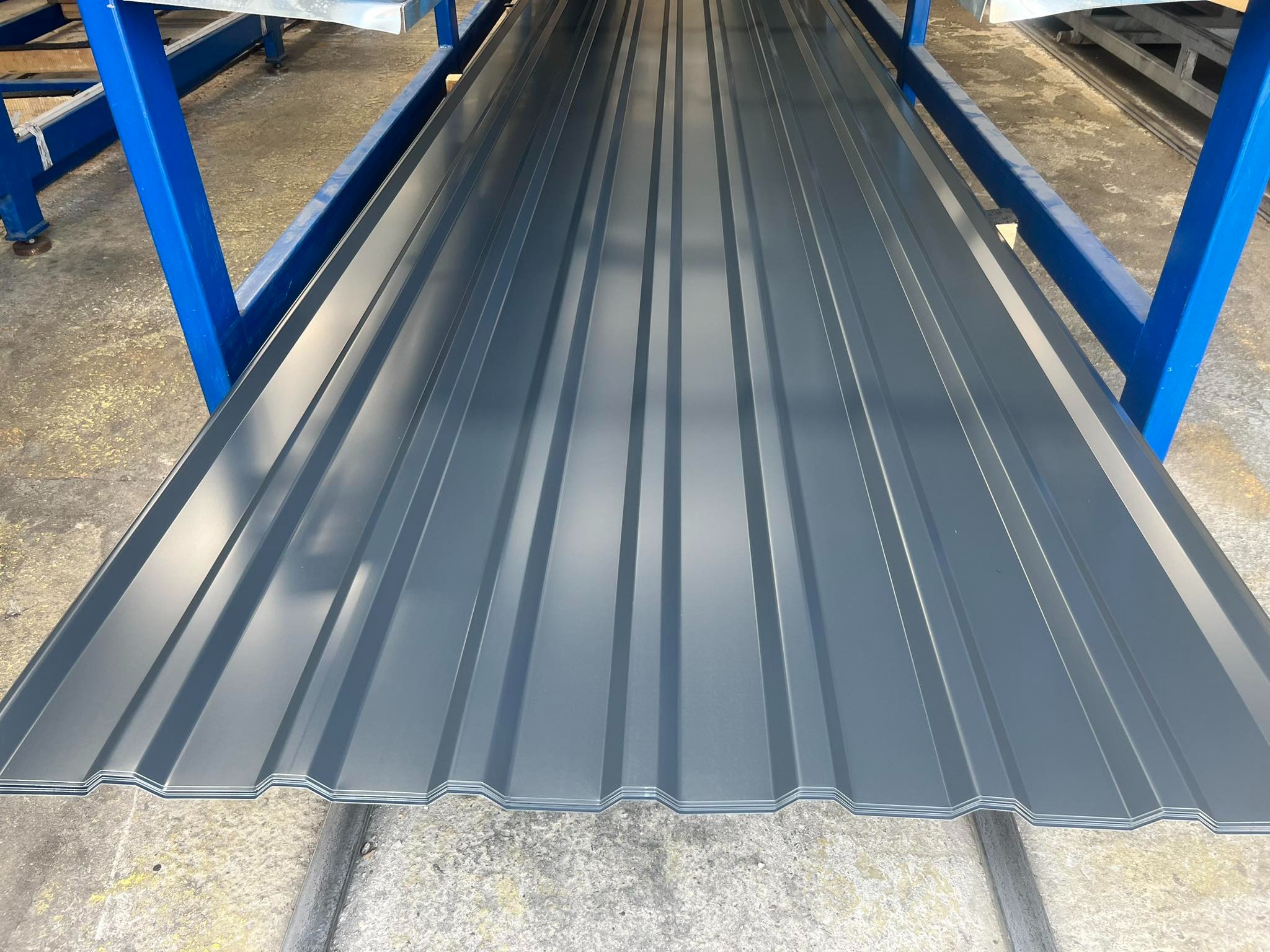 Szara blacha trapezowa na metalowej konstrukcji. Widok z góry ukazuje profilowane arkusze, gotowe do montażu. Minimalistyczne ujęcie podkreśla geometrię materiału.