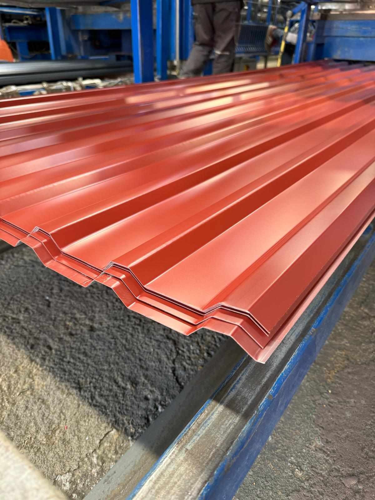 Czerwona blacha trapezowa ułożona warstwowo na konstrukcji. Widoczne charakterystyczne przetłoczenia i połyskliwa powierzchnia. Materiał gotowy do montażu na dachu.