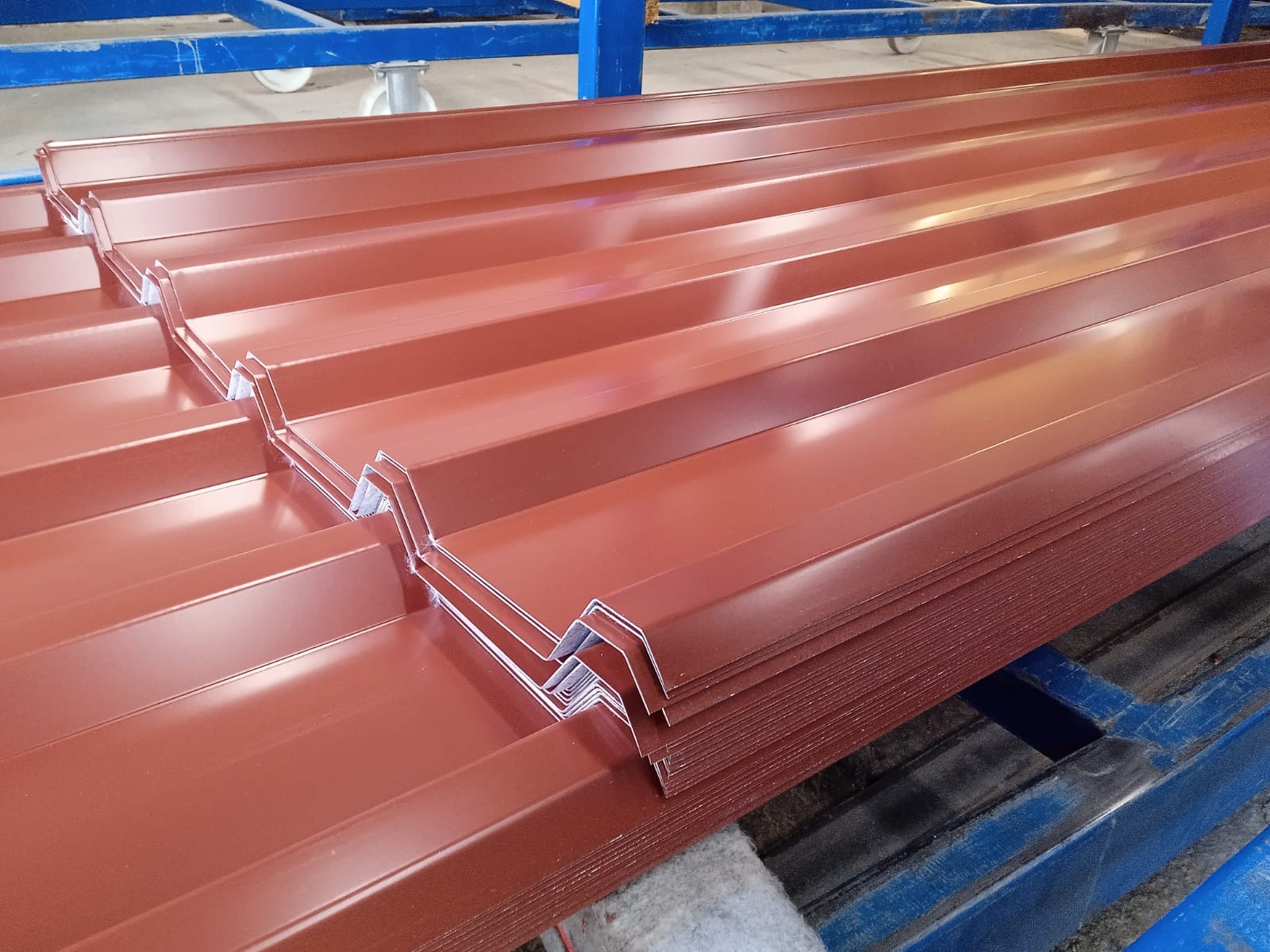 Stos brązowej blachy trapezowej na niebieskim regale w Lubinie. Widoczne charakterystyczne przetłoczenia i krawędzie arkuszy. Materiał przygotowany do transportu.