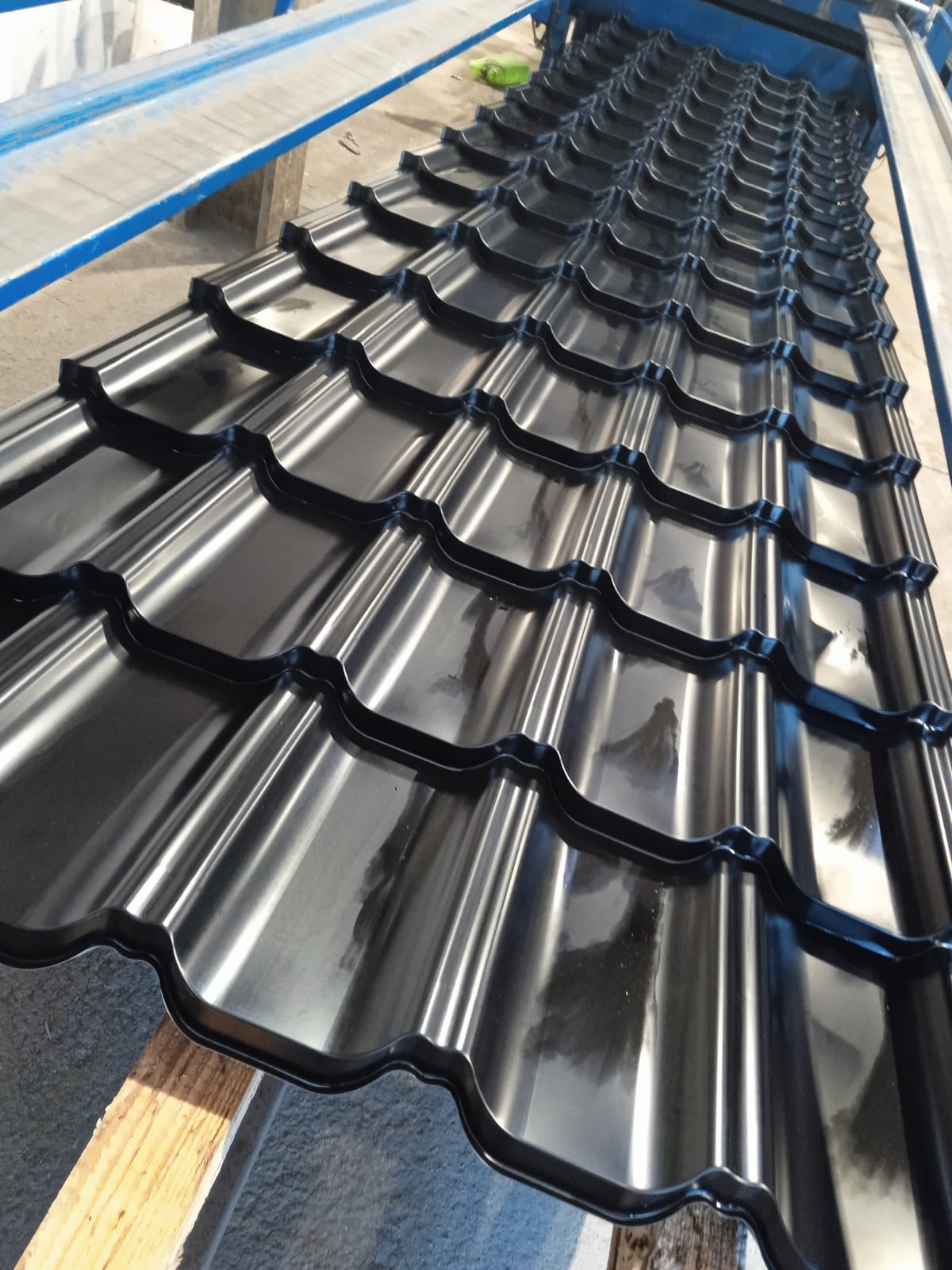 Błyszcząca, czarna blacha dachowa w kształcie dachówki, ułożona na drewnianych legarach. Widoczne odbicia światła na powierzchni blachy.