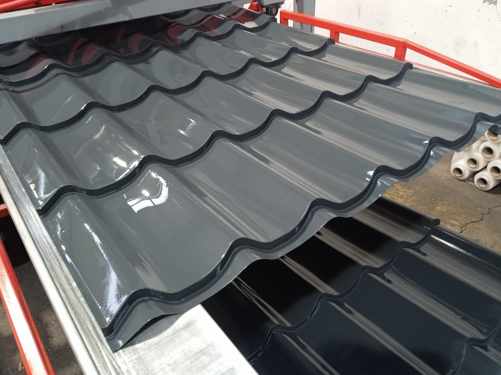 Błyszczące, szare dachówki ceramiczne w zbliżeniu, ułożone warstwami na metalowej konstrukcji. Widoczne detale falistego kształtu i gładkiej powierzchni.