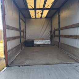 Usługi Transportowe RALF-PORT RAFAŁ CZOIK - Wnętrze paki busa transportowego z drewnianymi listwami zabezpieczającymi, oświetleniem dachowym i ładunkiem w postaci opon i płyt.