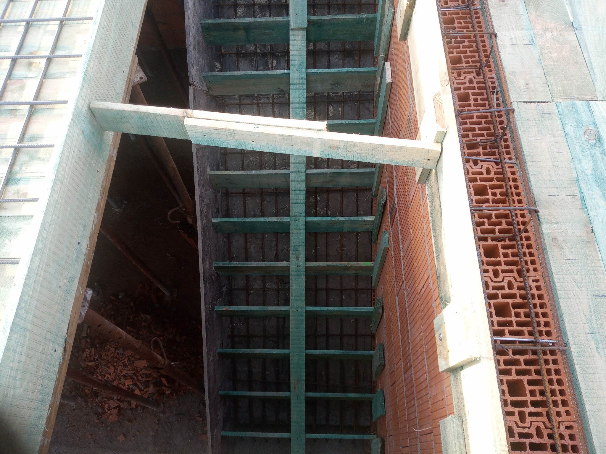 Zbrojenie fundamentów z drewnianym szalunkiem i pustakami ceramicznymi. Widok z góry na przygotowany wykop pod budynek. Elementy konstrukcyjne w kolorze zielonym.