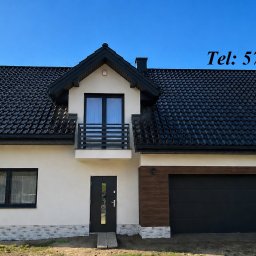 Elewacje, docieplenia budynków, ocieplenia domów - TERMI Mariusz Żurek - Nowoczesny dom jednorodzinny z czarnym dachem i garażem, jasna elewacja z elementami dekoracyjnymi imitującymi kamień. Widoczny numer domu i samochód na podjeździe.