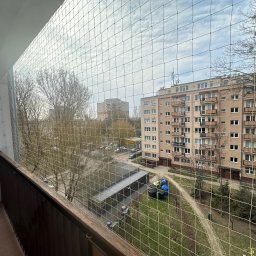 Ivan Lukashuk - Zabezpieczenie balkonu siatką ochronną, widok z góry na osiedle mieszkaniowe. Siatka zamontowana na drewnianej balustradzie. Dzień, pochmurne niebo.