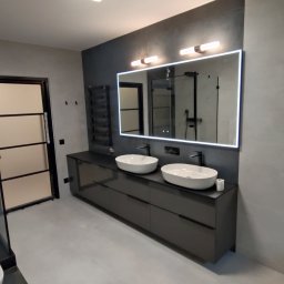 A.R.M. - Elegancka łazienka: podwójna, owalna umywalka na ciemnoszarej, lakierowanej szafce. Duże lustro z podświetleniem LED, czarny grzejnik drabinkowy na szarej ścianie i jasnoszare płytki.
