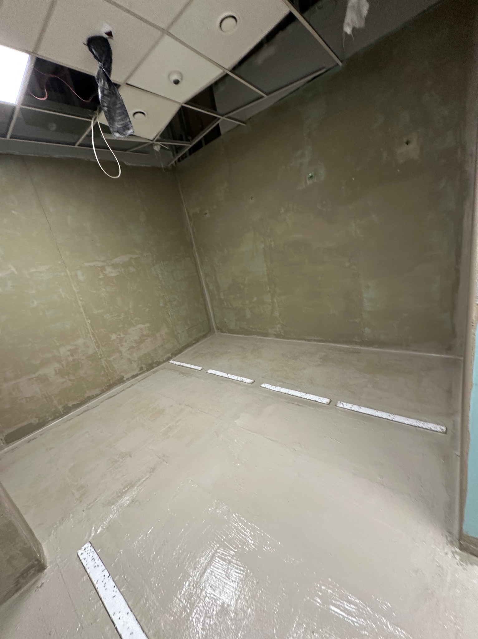 Świeżo wylana, mokra wylewka samopoziomująca w pomieszczeniu z przygotowanymi ścianami. Widoczne listwy dylatacyjne i niedokończony sufit podwieszany.