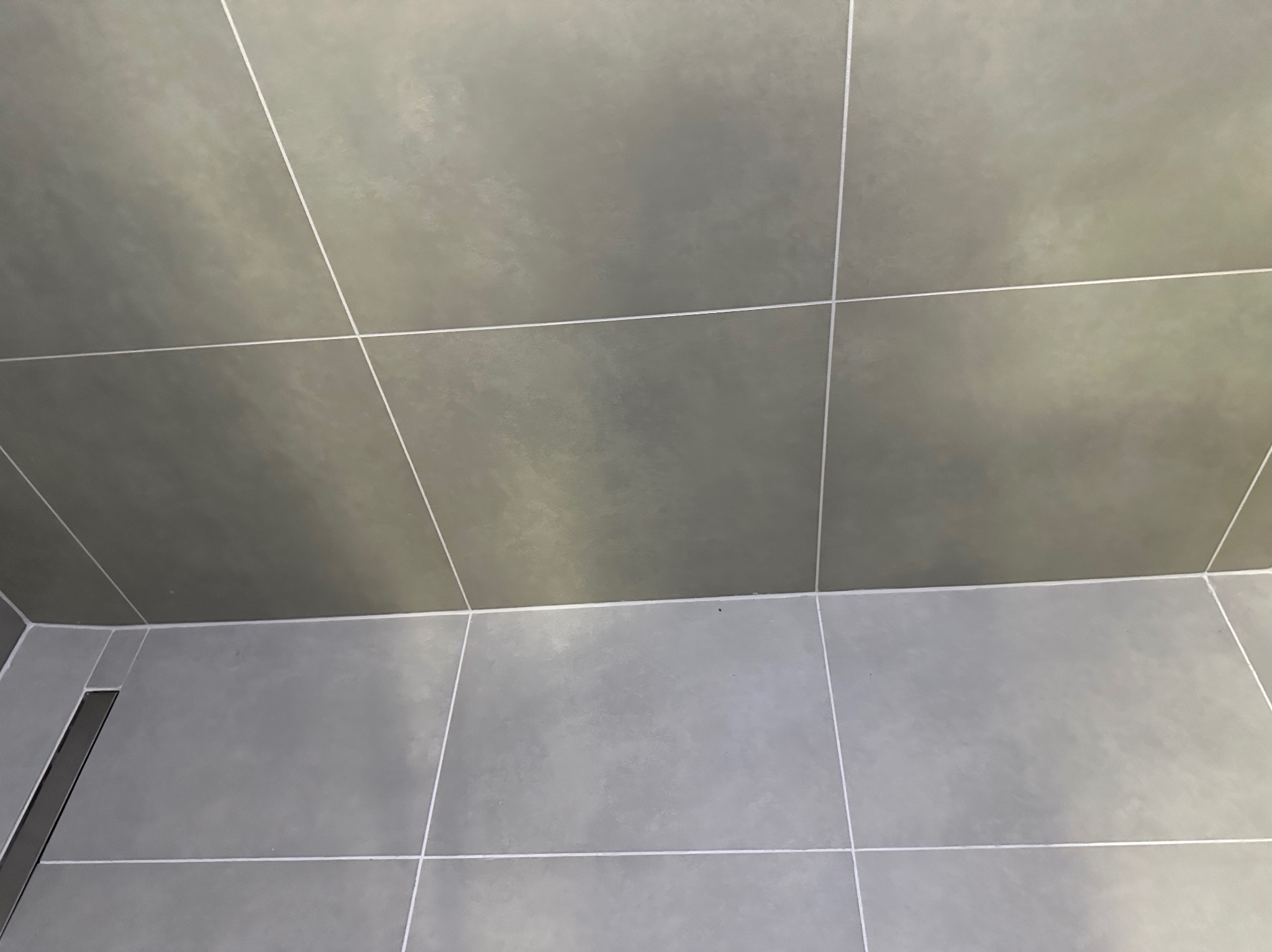 Szare, matowe płytki podłogowe i ścienne z fugami w łazience w Rudzie Śląskiej. Widoczny odpływ liniowy przy ścianie. Minimalistyczny design, neutralna kolorystyka.