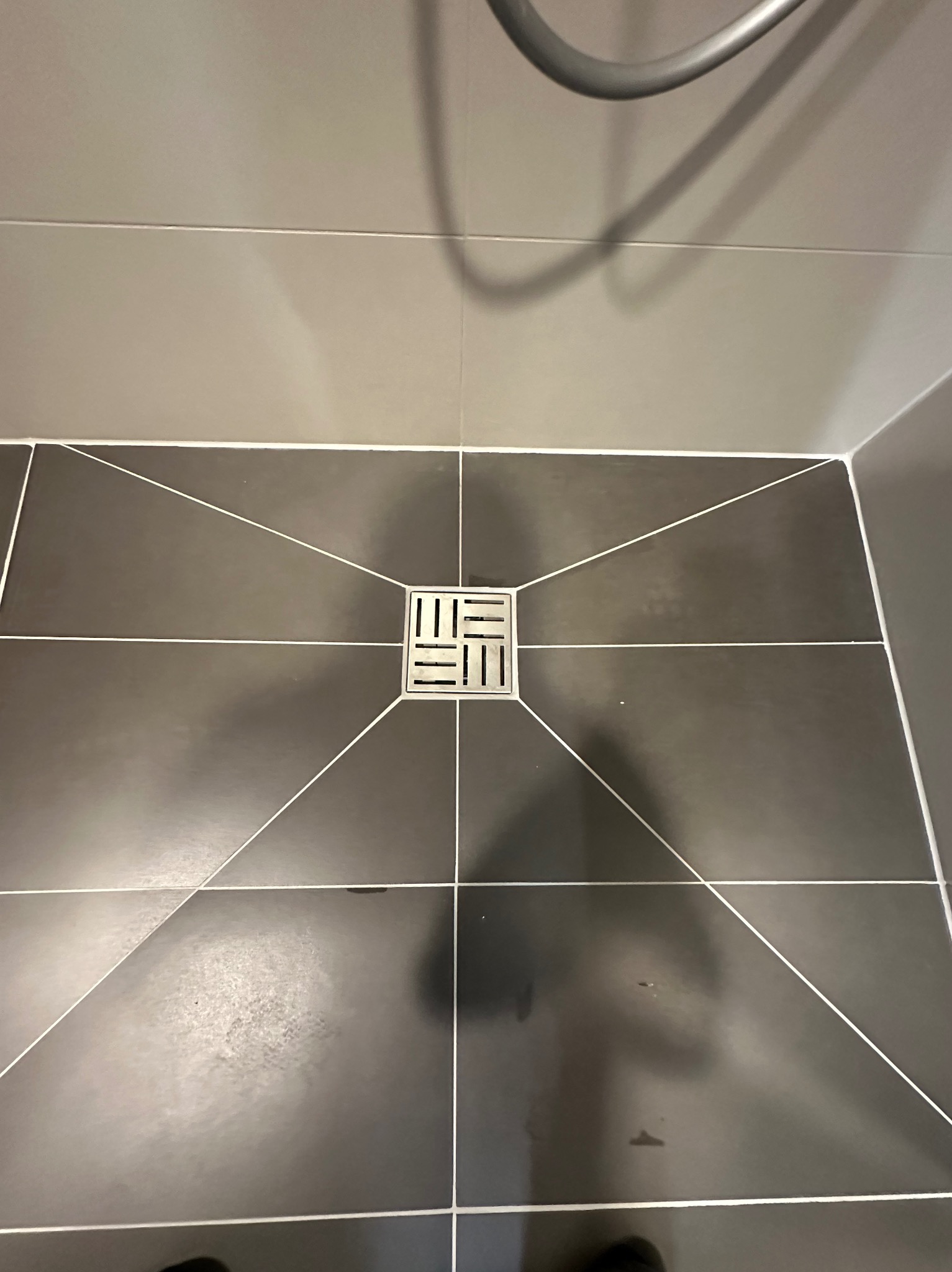 Nowoczesna łazienka: ciemne płytki podłogowe z kwadratowym odpływem liniowym i jasnymi fugami, widok z góry, fragment kabiny prysznicowej.