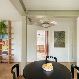 Anna Komorowicz Studio - Jasne wnętrze mieszkania z drewnianym regałem, okrągłym stołem z owocami i widokiem na dalszą część domu. Minimalistyczny design, parkiet w jodełkę.