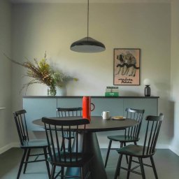 Anna Komorowicz Studio - Nowoczesna kuchnia z okrągłym stołem i czarnymi krzesłami. Na stole czerwony dzbanek i biały kubek. W tle plakat i kwiaty w wazonie na tle szafek.