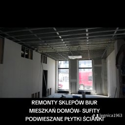 Janusz Goluch - Montaż płyt G-K na metalowym stelażu sufitu podwieszanego w remontowanym pomieszczeniu biurowym. Widoczne okna i fragment ściany z nałożoną gładzią.