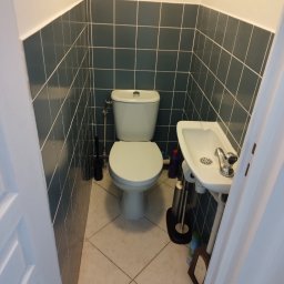 Łukasz - Wykończona łazienka w Police z toaletą, umywalką i ciemnymi płytkami na ścianach. Widok zza uchylonych drzwi.