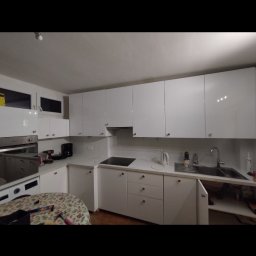 Łukasz - Biała, nowoczesna kuchnia z błyszczącymi frontami szafek, widok na blat z kuchenką i zlewem. Na stole narzędzia i akcesoria, sugerujące prace wykończeniowe.