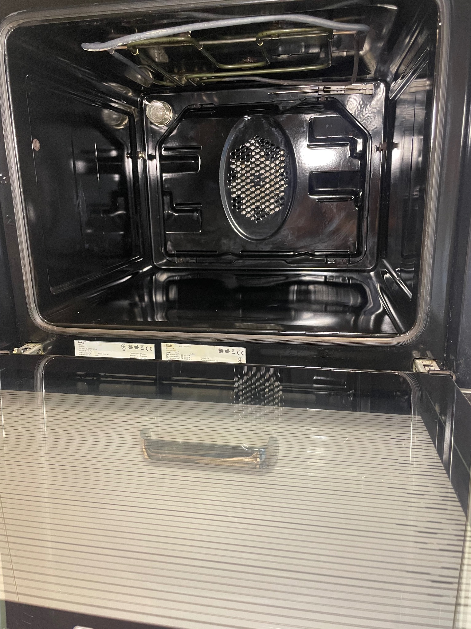 Wnętrze czarnego piekarnika z otwartymi drzwiczkami, widoczne elementy grzejne i oświetlenie. Piekarnik marki Beko z widocznymi etykietami informacyjnymi.