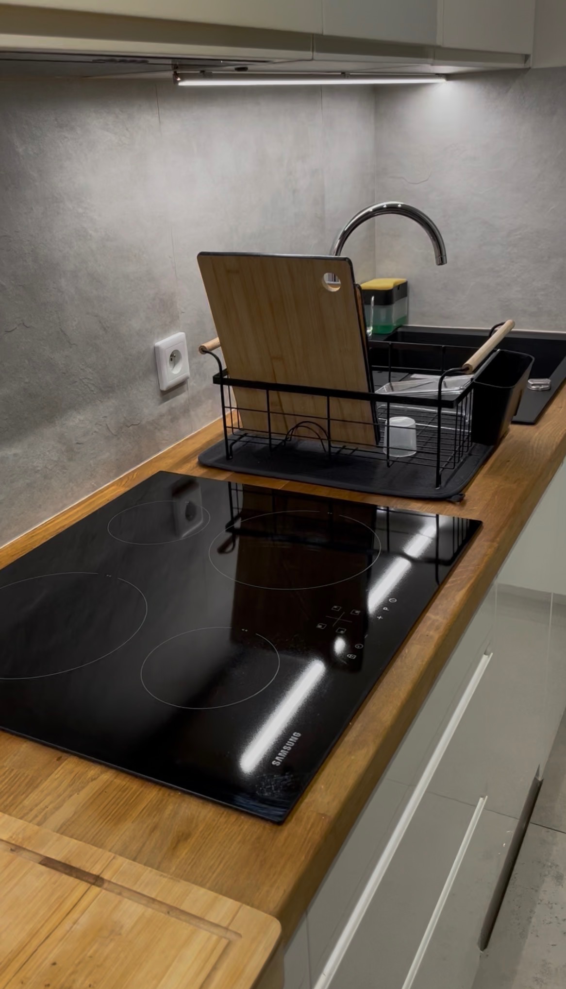 Umyta płyta indukcyjna Samsung i czysty zlew z ociekaczem na blacie drewnianym w minimalistycznej kuchni po sprzątaniu. Widoczny dozownik na płyn i gąbka.